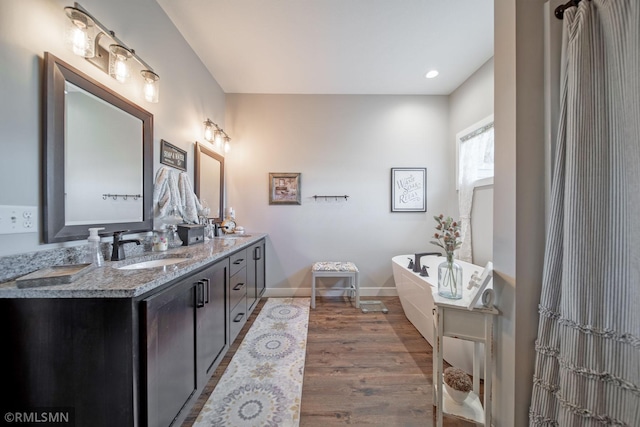 bathroom with wood-type flooring, a bath, and vanity