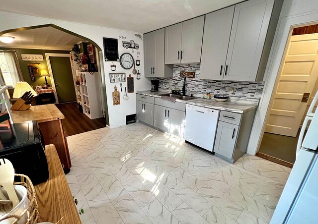 kitchen with white dishwasher, sink, tasteful backsplash, gray cabinets, and light wood-type flooring