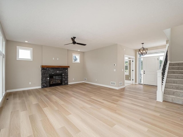 unfurnished living room with ceiling fan, a stone fireplace, and light wood-type flooring