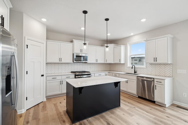 kitchen featuring a kitchen island, appliances with stainless steel finishes, sink, white cabinets, and hanging light fixtures