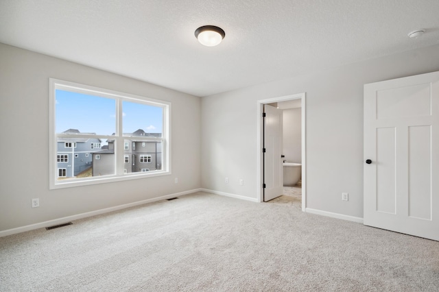 unfurnished bedroom featuring ensuite bathroom, light carpet, and a textured ceiling