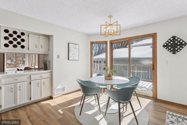 dining area featuring a notable chandelier, visible vents, a textured ceiling, light wood-type flooring, and baseboards