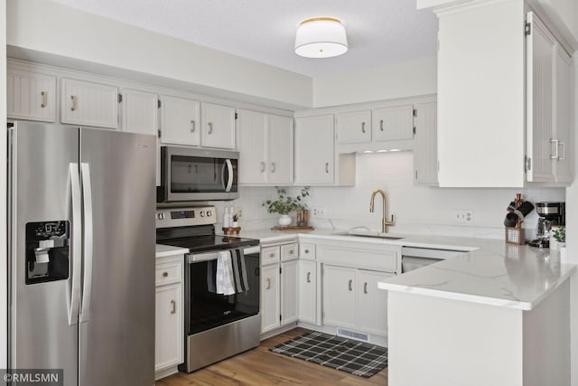 kitchen with decorative backsplash, appliances with stainless steel finishes, white cabinets, a sink, and wood finished floors