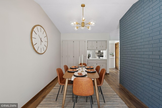 dining room with an accent wall, dark wood-style flooring, brick wall, and an inviting chandelier