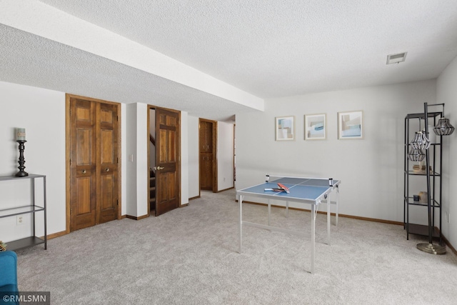 rec room with light colored carpet, a textured ceiling, and baseboards