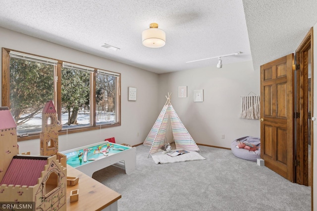 recreation room featuring carpet, visible vents, a textured ceiling, track lighting, and baseboards