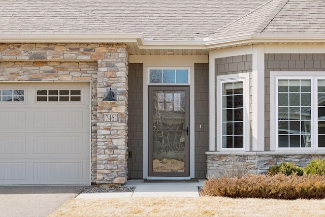 view of exterior entry featuring stone siding, an attached garage, and a shingled roof