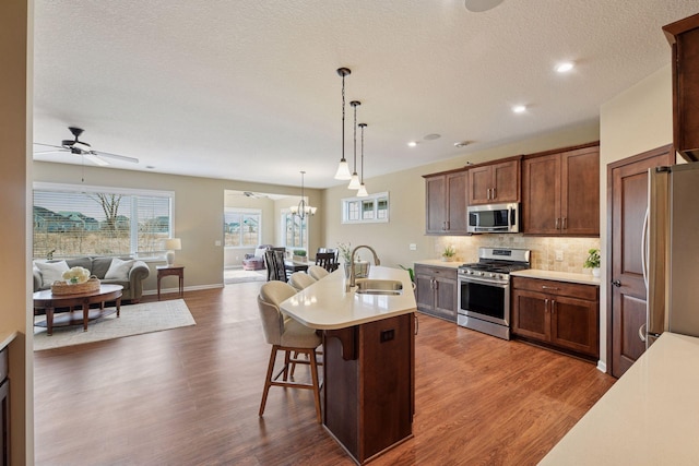 kitchen featuring a sink, tasteful backsplash, open floor plan, appliances with stainless steel finishes, and light countertops