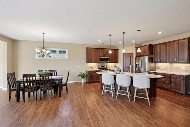 kitchen with dark wood-type flooring, a center island with sink, stainless steel appliances, light countertops, and a chandelier