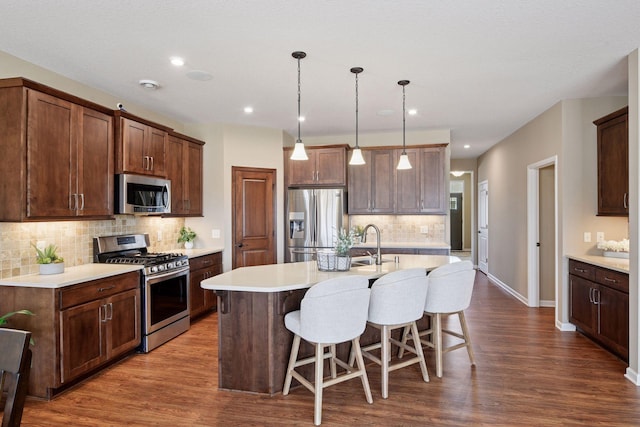 kitchen featuring light countertops, appliances with stainless steel finishes, a kitchen breakfast bar, dark wood-style floors, and a kitchen island with sink