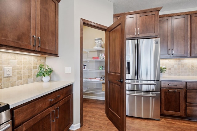 kitchen with stainless steel fridge with ice dispenser, dark brown cabinetry, light countertops, light wood-type flooring, and decorative backsplash