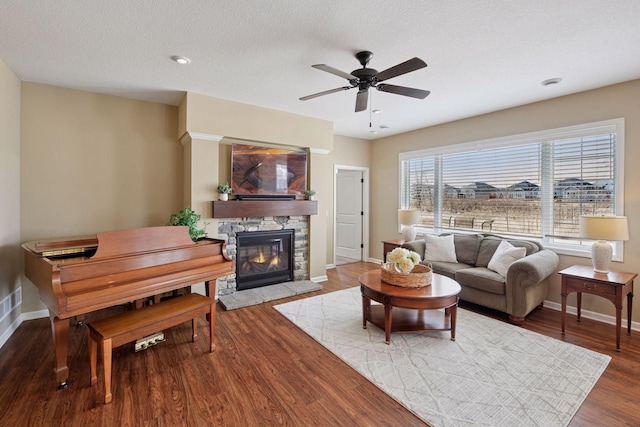 living area featuring baseboards, a fireplace, wood finished floors, a textured ceiling, and a ceiling fan