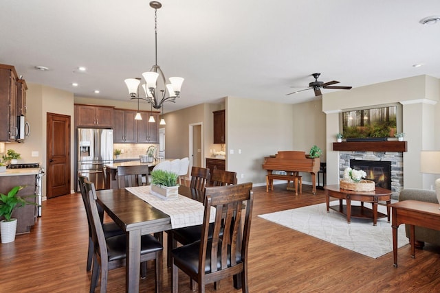 dining room featuring dark wood-style floors, baseboards, recessed lighting, a fireplace, and ceiling fan with notable chandelier