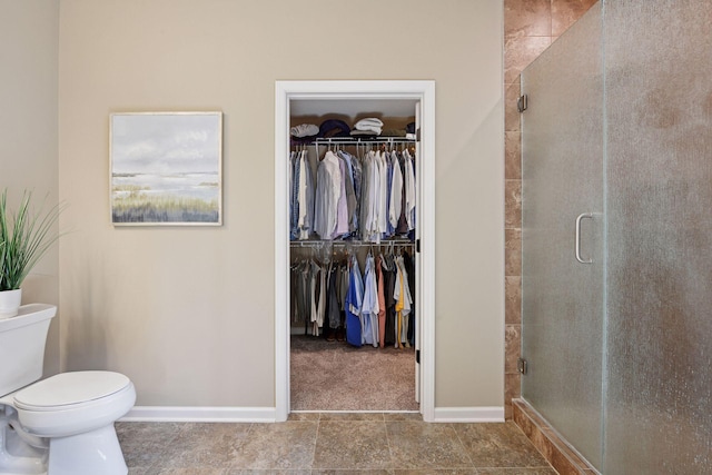 full bathroom featuring a walk in closet, toilet, baseboards, and a stall shower