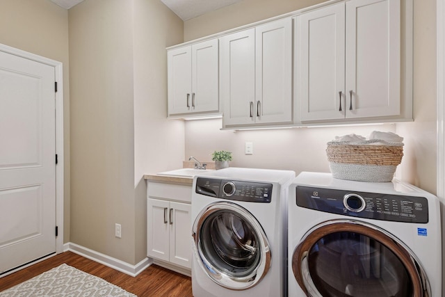 washroom with wood finished floors, baseboards, washing machine and clothes dryer, cabinet space, and a sink