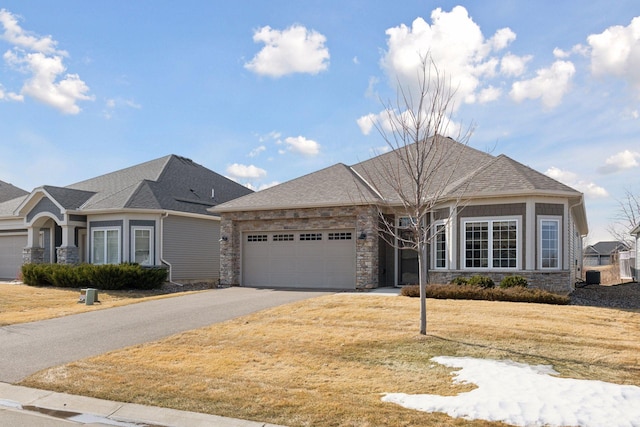 view of front of home featuring a shingled roof, aphalt driveway, a front yard, a garage, and stone siding