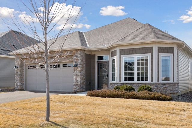 view of front of home featuring a front yard, an attached garage, a shingled roof, concrete driveway, and stone siding