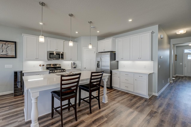 kitchen with stainless steel appliances, a sink, white cabinetry, light countertops, and a center island with sink