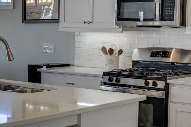 kitchen with appliances with stainless steel finishes, backsplash, light countertops, white cabinetry, and a sink