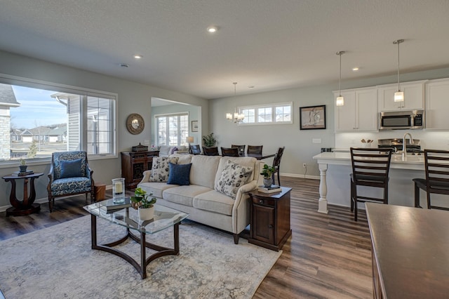 living room with a textured ceiling, a chandelier, recessed lighting, baseboards, and dark wood-style floors