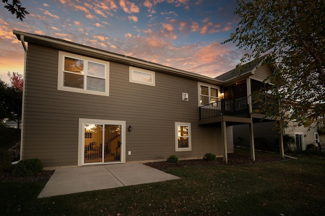 back house at dusk with a lawn, a balcony, and a patio area