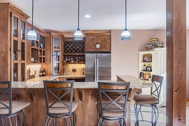 kitchen featuring decorative backsplash, a kitchen bar, hanging light fixtures, and stainless steel refrigerator