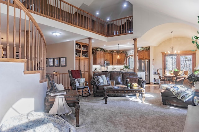 carpeted living room featuring an inviting chandelier, decorative columns, and high vaulted ceiling