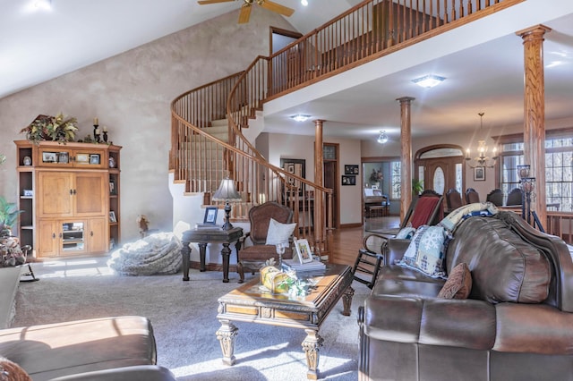 carpeted living room with high vaulted ceiling, decorative columns, and ceiling fan with notable chandelier