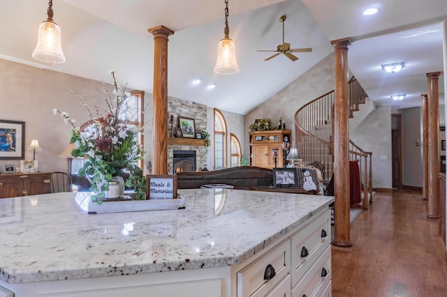 kitchen featuring dark wood-type flooring, lofted ceiling, decorative columns, hanging light fixtures, and light stone countertops