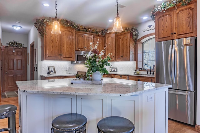 kitchen featuring appliances with stainless steel finishes, a kitchen island, light stone countertops, and pendant lighting