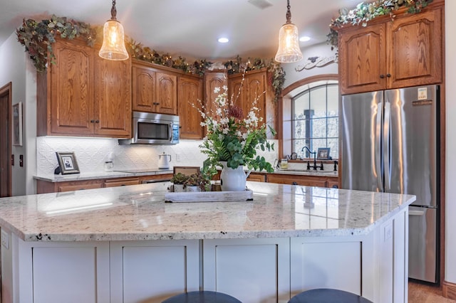 kitchen featuring appliances with stainless steel finishes, a kitchen island, light stone countertops, pendant lighting, and sink