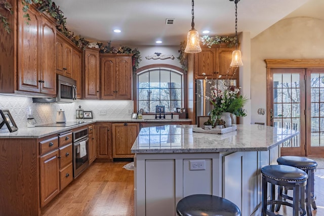 kitchen with decorative light fixtures, stainless steel appliances, a center island, light hardwood / wood-style floors, and decorative backsplash