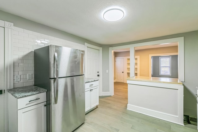 kitchen featuring stainless steel fridge, light wood-type flooring, light stone countertops, backsplash, and white cabinets