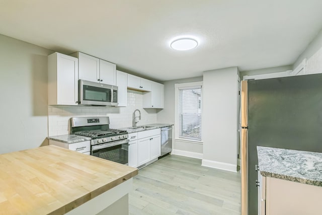 kitchen featuring sink, white cabinetry, light hardwood / wood-style flooring, appliances with stainless steel finishes, and backsplash