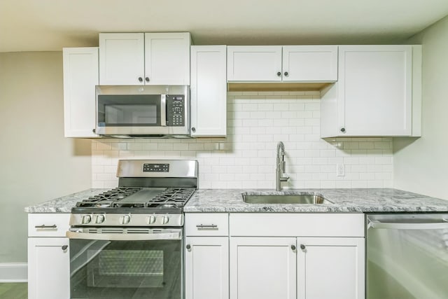 kitchen with sink, light stone counters, backsplash, appliances with stainless steel finishes, and white cabinetry