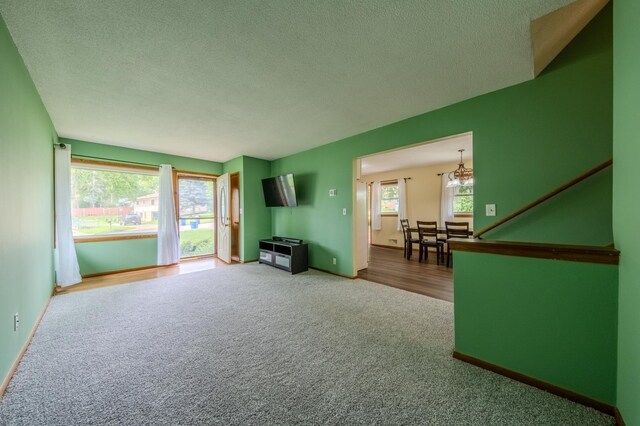 unfurnished living room with carpet flooring, a textured ceiling, and a notable chandelier