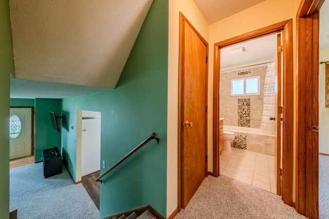 corridor with lofted ceiling, light colored carpet, and a textured ceiling