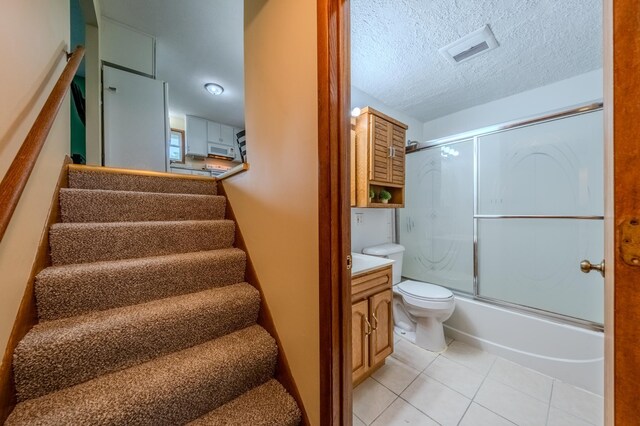 full bathroom featuring tile patterned floors, bath / shower combo with glass door, a textured ceiling, vanity, and toilet