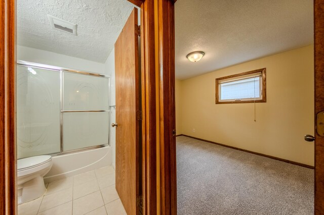 bathroom with tile patterned flooring, a textured ceiling, toilet, and bath / shower combo with glass door