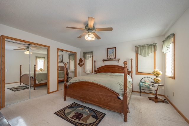 bedroom with ceiling fan, light colored carpet, a textured ceiling, and two closets