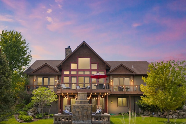 back house at dusk featuring a wooden deck and a lawn