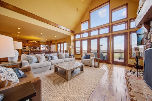 living room with a towering ceiling, a notable chandelier, french doors, and light hardwood / wood-style flooring