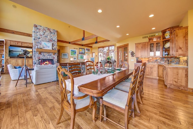 dining room with sink, light wood-type flooring, beamed ceiling, and a stone fireplace