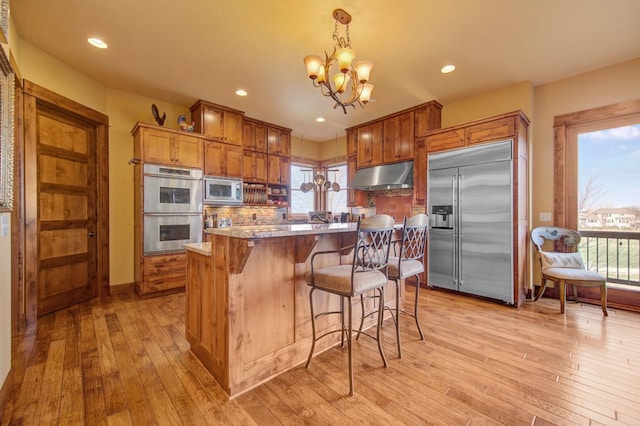 kitchen featuring built in appliances, light stone counters, light hardwood / wood-style flooring, a chandelier, and pendant lighting