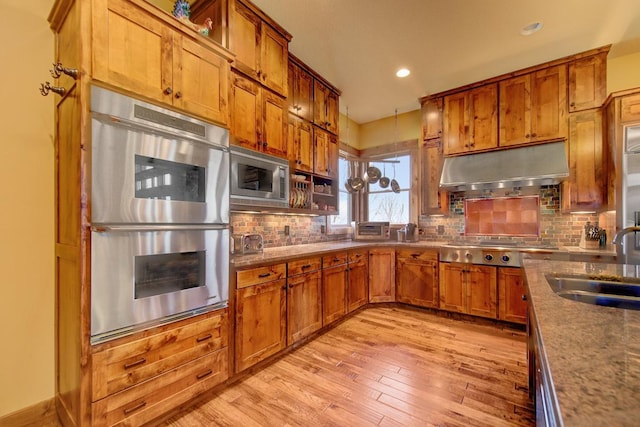 kitchen with appliances with stainless steel finishes, light hardwood / wood-style floors, decorative backsplash, and sink