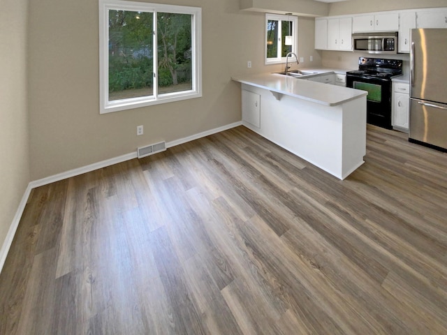 kitchen with white cabinets, kitchen peninsula, stainless steel appliances, hardwood / wood-style floors, and sink