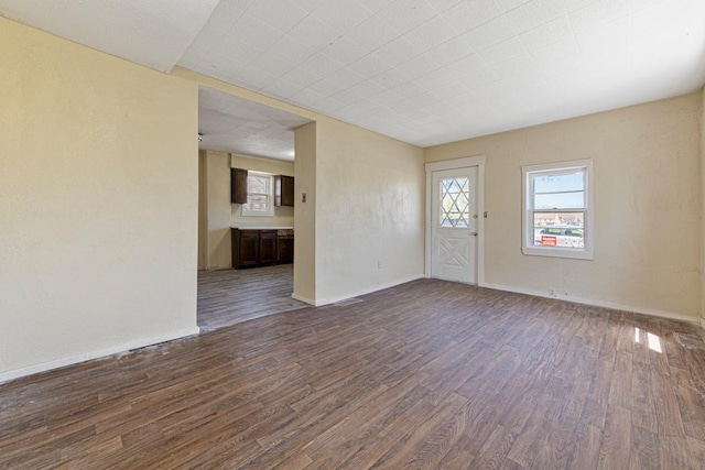 unfurnished living room with baseboards, dark wood-style flooring, and visible vents