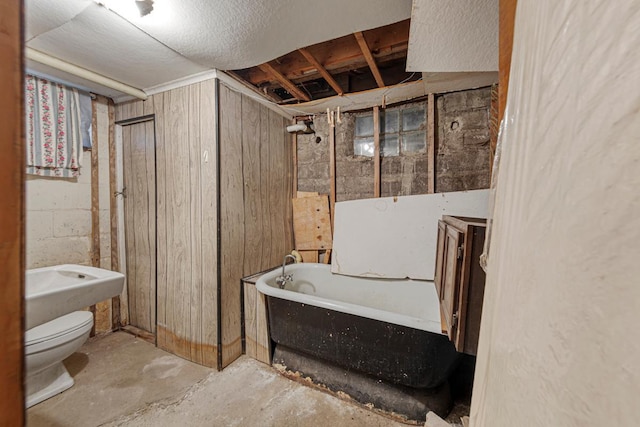 full bath featuring a tub to relax in, wooden walls, toilet, and unfinished concrete floors