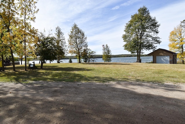 view of yard with a garage, a water view, and an outbuilding