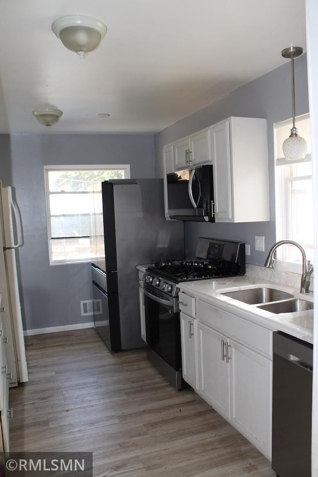 kitchen with white cabinetry, sink, black appliances, decorative light fixtures, and light hardwood / wood-style flooring